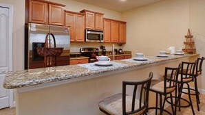 A kitchen with wooden cabinets, a granite countertop, and a bar area with stools. - Paradise Palms 8967 D (Kissimmee)