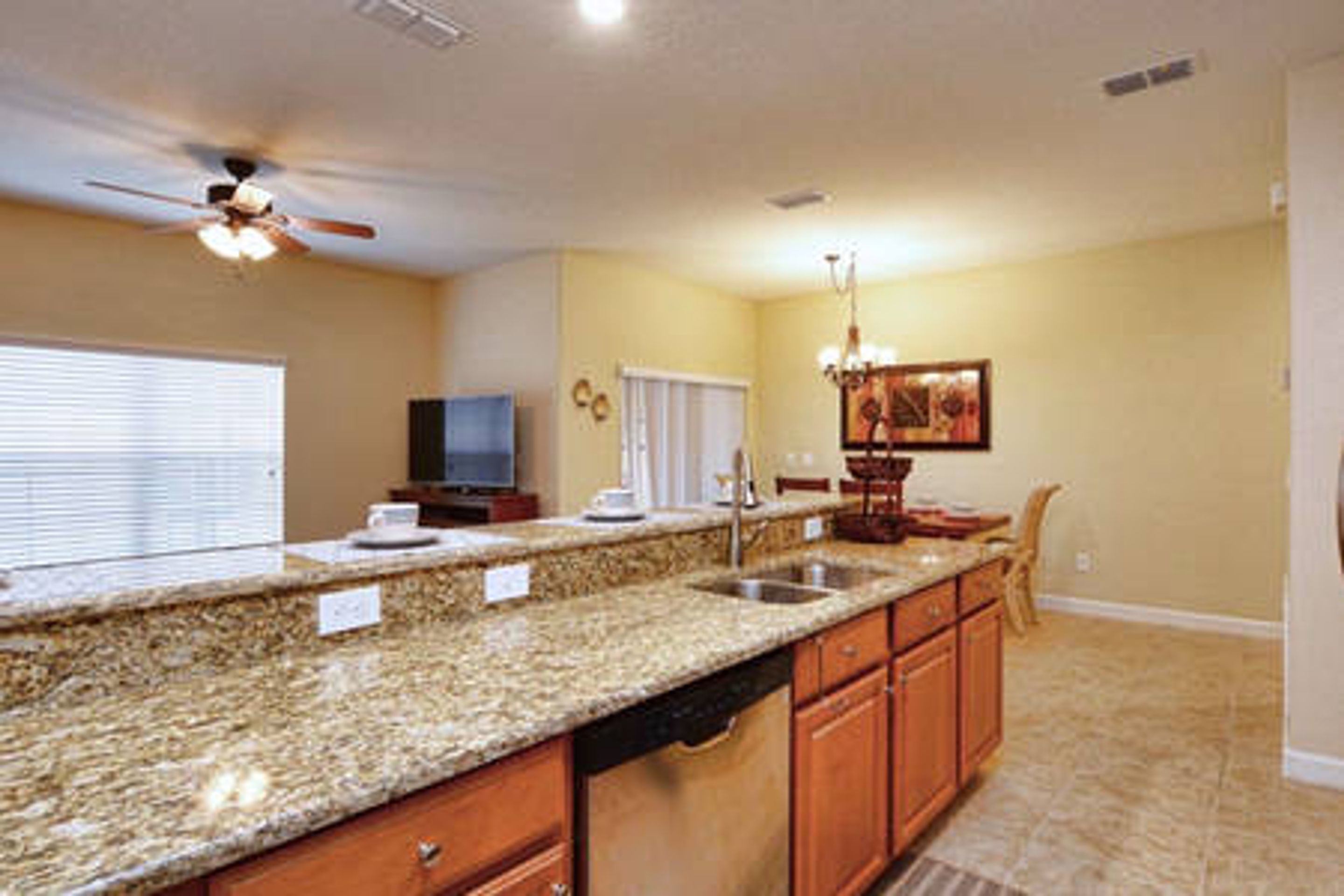 A kitchen with granite countertops, wooden cabinets, a dishwasher, a ceiling fan, and a chandelier.