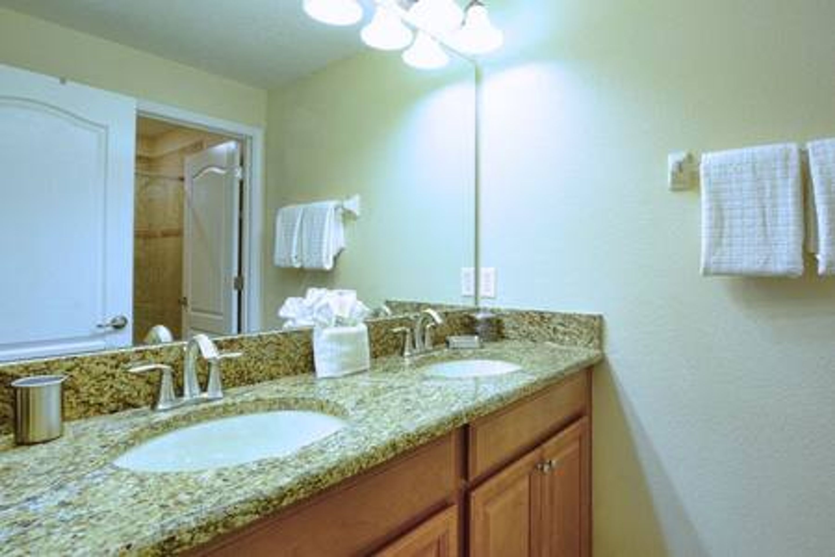 A bathroom with a granite countertop, two sinks, a mirror, and a towel rack.