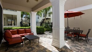 Un patio cubierto con un sofá rojo, una mesa, sillas, un paraguas rojo y una escalera que sube a un nivel superior.