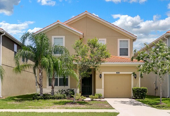 A two-story residential house with a beige exterior, a red-tiled roof, and a front garage.