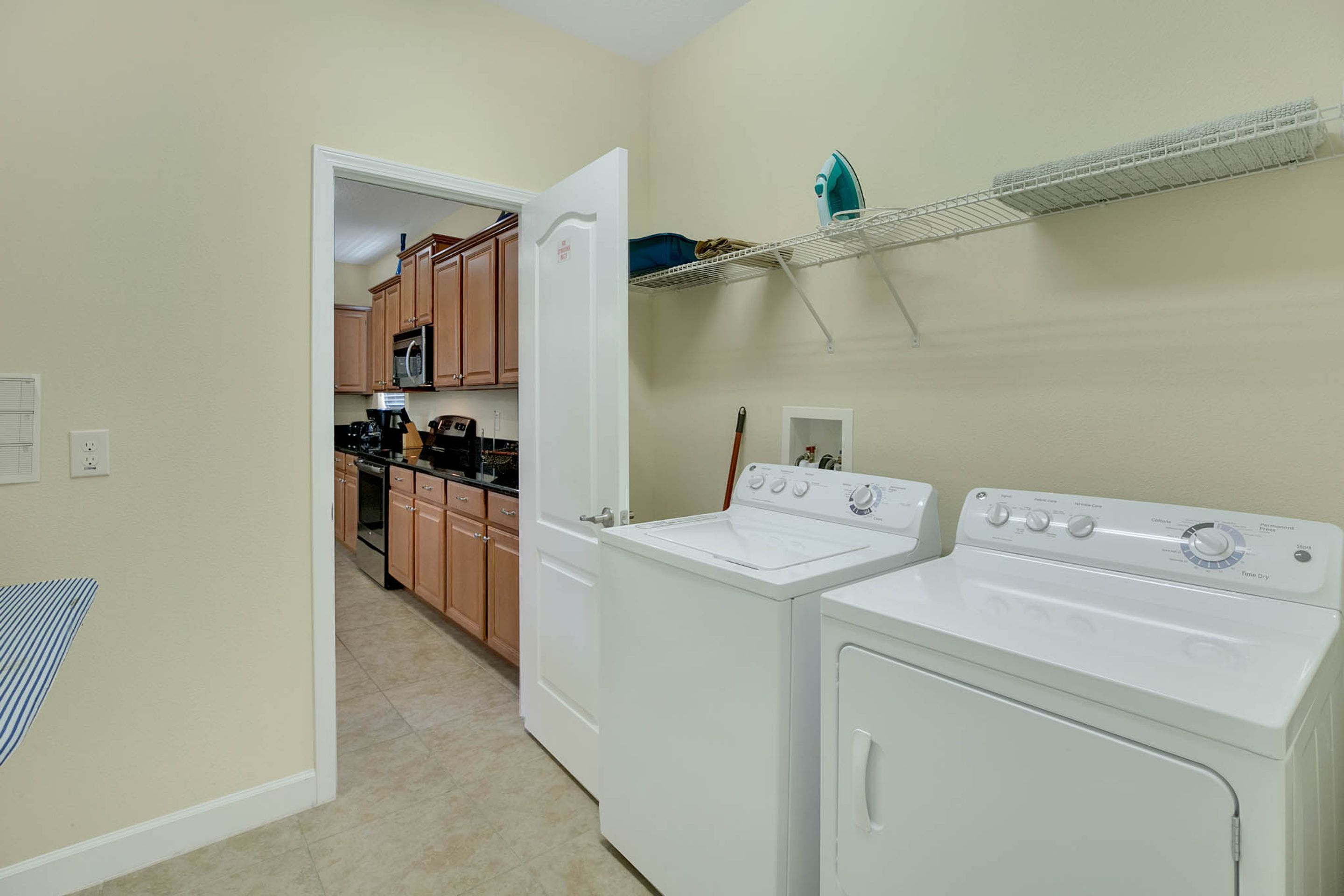 A laundry room with two white washers and dryers, wooden cabinets, and a metal shelf above the dryers.