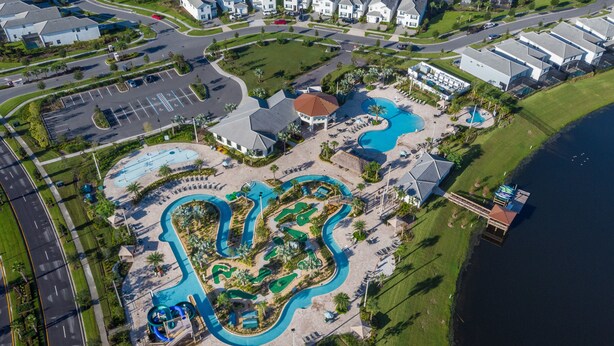 An aerial view of a resort with multiple swimming pools, a parking lot, and a body of water. - Storey Lake 4813 (Kissimmee)