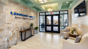 A lobby with a stone wall, a reception desk, two sofas, and a TV mounted on the wall. - Storey Lake 4813 (Kissimmee)