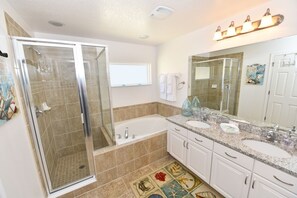 A bathroom with a glass-enclosed shower, a bathtub, two sinks, and a large mirror. - Watersong Resort 427 (Davenport)