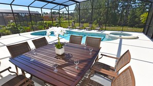 An outdoor patio with a wooden table and wicker chairs, overlooking a swimming pool and lush greenery. - Watersong Resort 427 (Davenport)