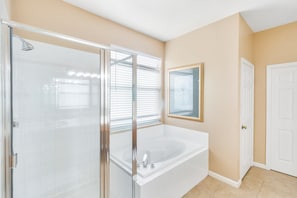 A bathroom with a glass shower enclosure, a white bathtub, and beige walls.