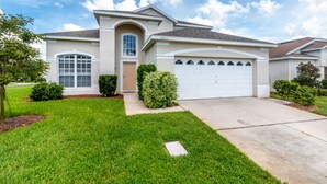 A single-story house with a garage, a front door, and a small front yard with grass and a few bushes. - Windsor Palms Resort 8017 (Kissimmee)