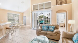 A spacious living area with a beige sofa, a glass coffee table, and a dining area with chairs and a table. - Windsor Palms Resort 8017 (Kissimmee)