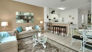 A modern living room with a sofa, coffee table, and a dining area with chairs and a glass table. - Windsor Palms Resort 2357 (Kissimmee)