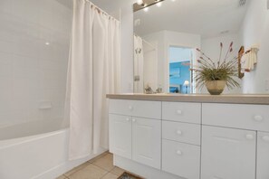 A bathroom with a bathtub, a shower curtain, a sink with a mirror, and a potted plant. - Windsor Palms Resort 2357 (Kissimmee)