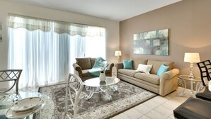 A living room with a sofa, two armchairs, a coffee table, and a dining table with chairs. There is a rug on the floor, a lamp on a side table, and a painting on the wall. - Windsor Palms Resort 2357 (Kissimmee)