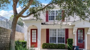 A two-story house with a red door, white shutters, and a small front yard with a tree and bushes. - Windsor Palms Resort 2357 (Kissimmee)