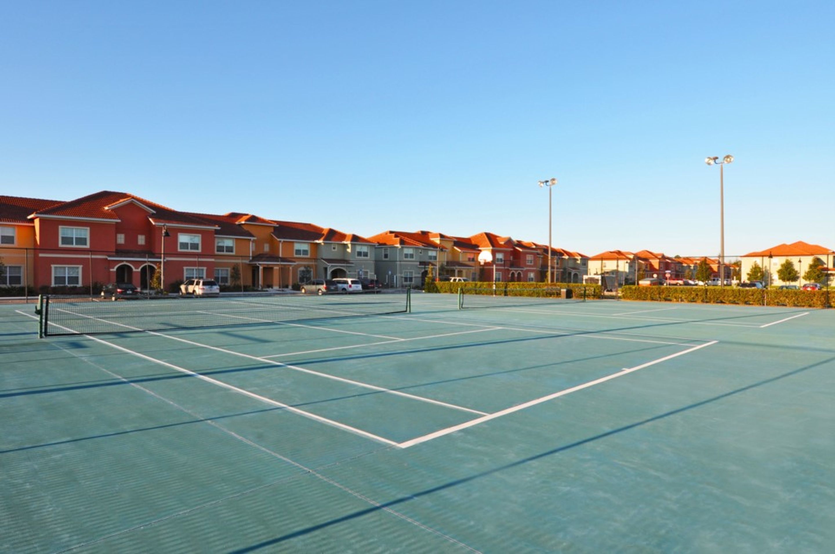 A tennis court with a net, surrounded by multi-story buildings with red roofs.