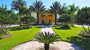 A well-maintained garden with a central pathway leading to a building with a yellow facade and arched entrance. - Paradise Palms 8963 C (Kissimmee)