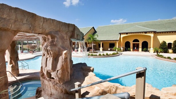 A pool area with a natural rock formation, a water feature, and a building with a green roof and arched windows. - Paradise Palms 8963 D (Kissimmee)