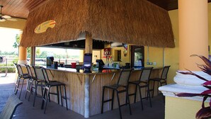 A bar area with a thatched roof, bar stools, and a counter with a coffee machine. - Paradise Palms 8963 D (Kissimmee)