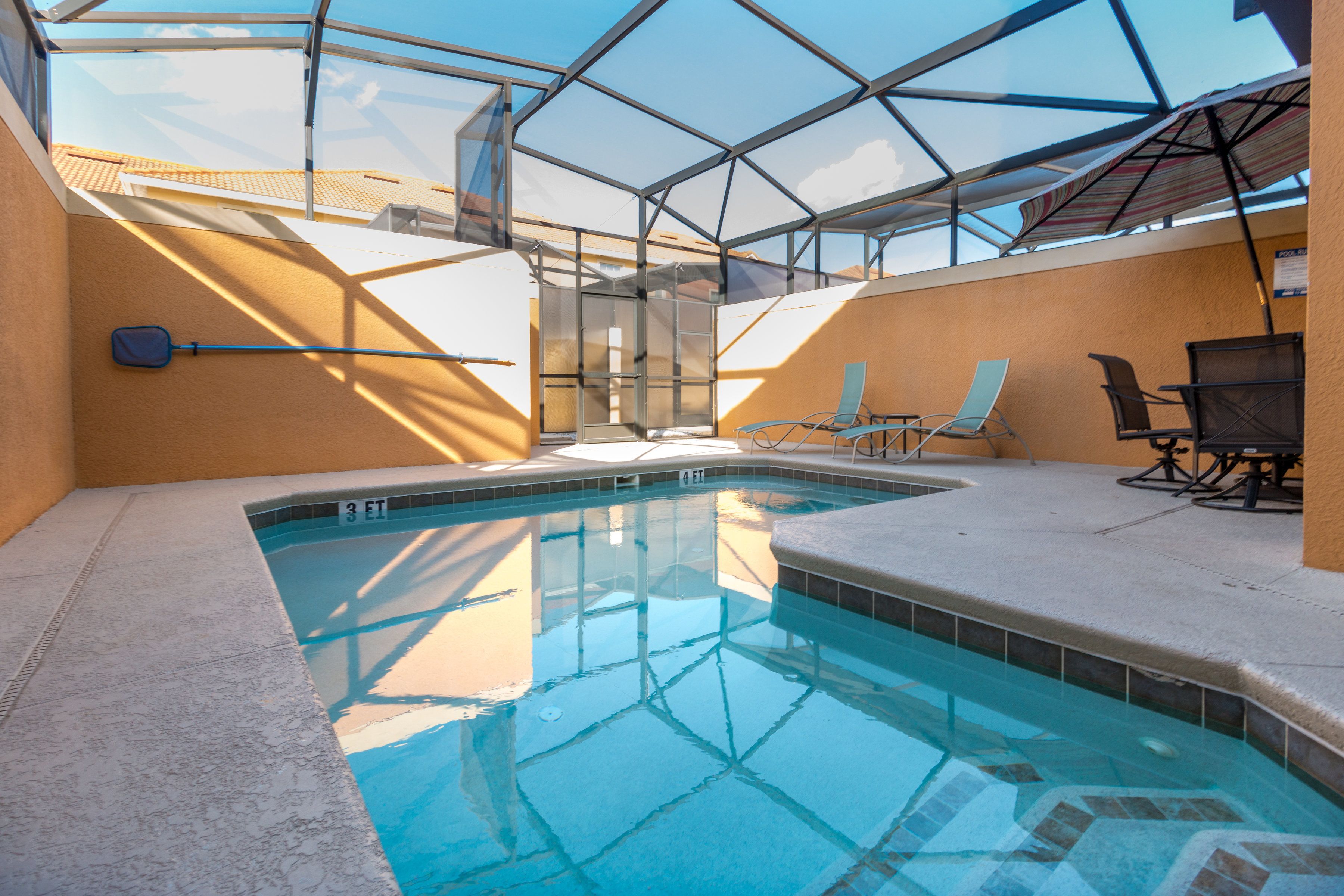 Une piscine intérieure avec des parois en verre transparent, un sol carrelé et quelques chaises longues.