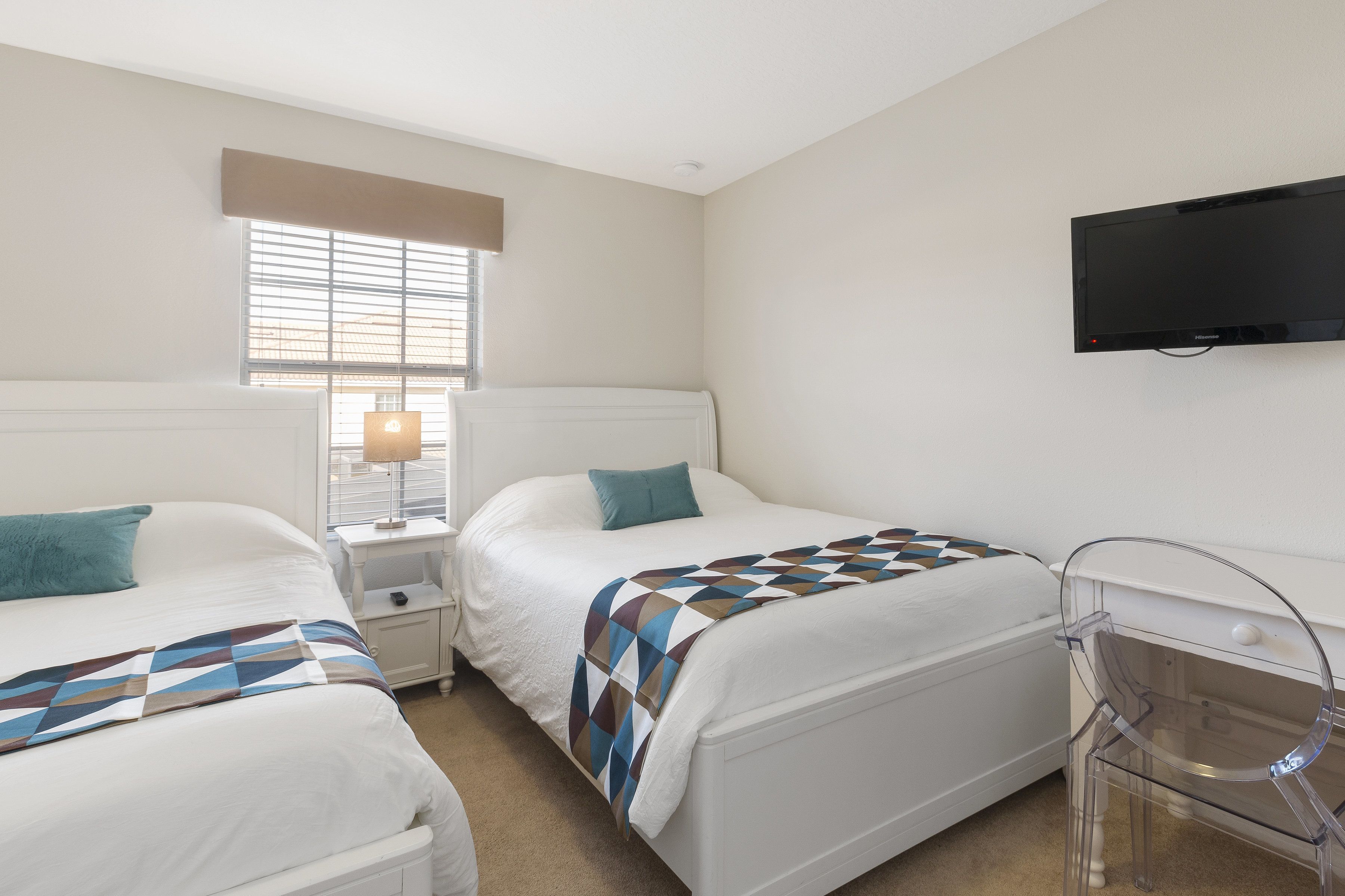 A hotel room with two beds, a TV mounted on the wall, and a desk with a chair.