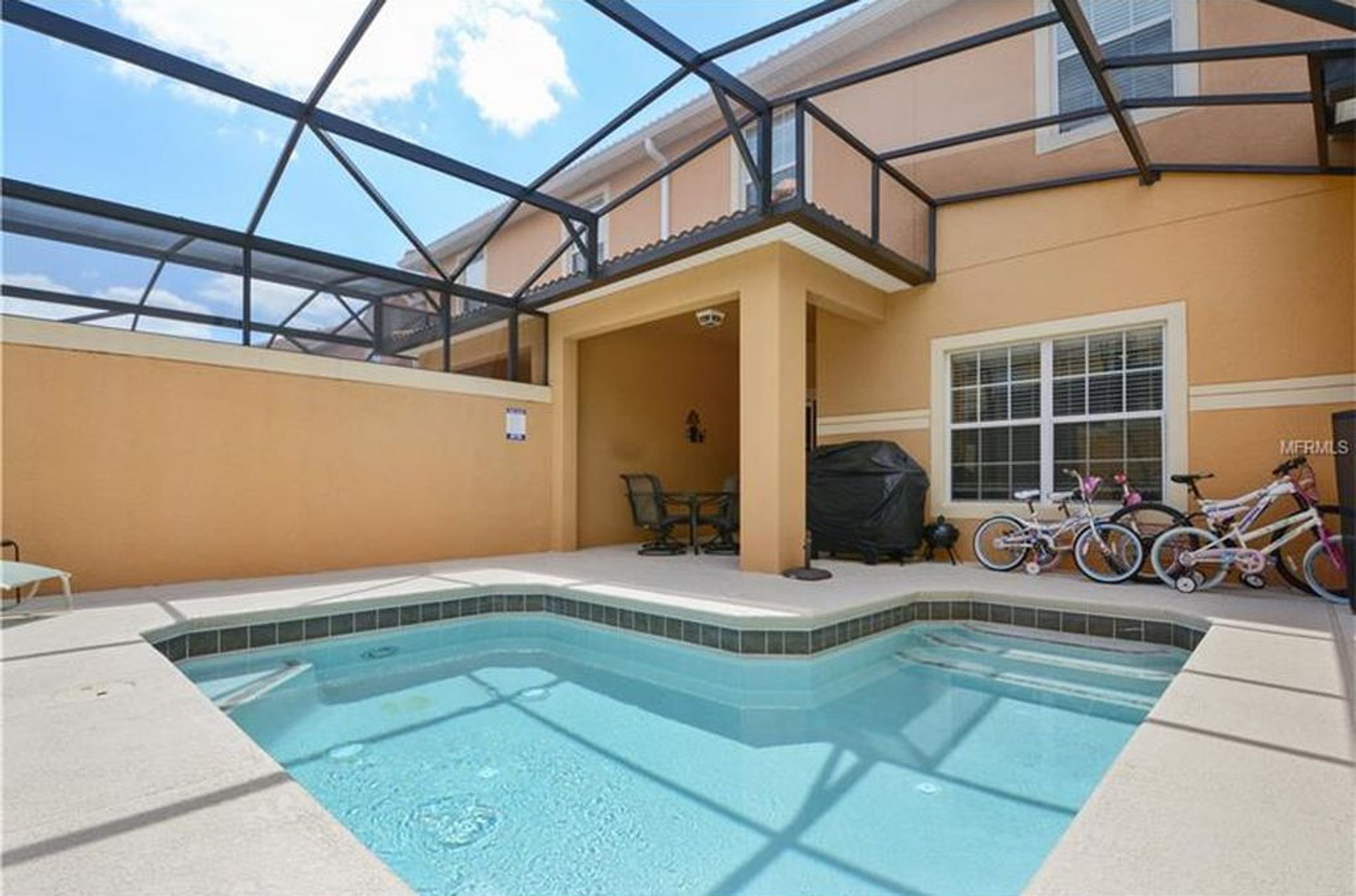 A swimming pool with a glass ceiling, a covered patio area, and bicycles parked nearby.