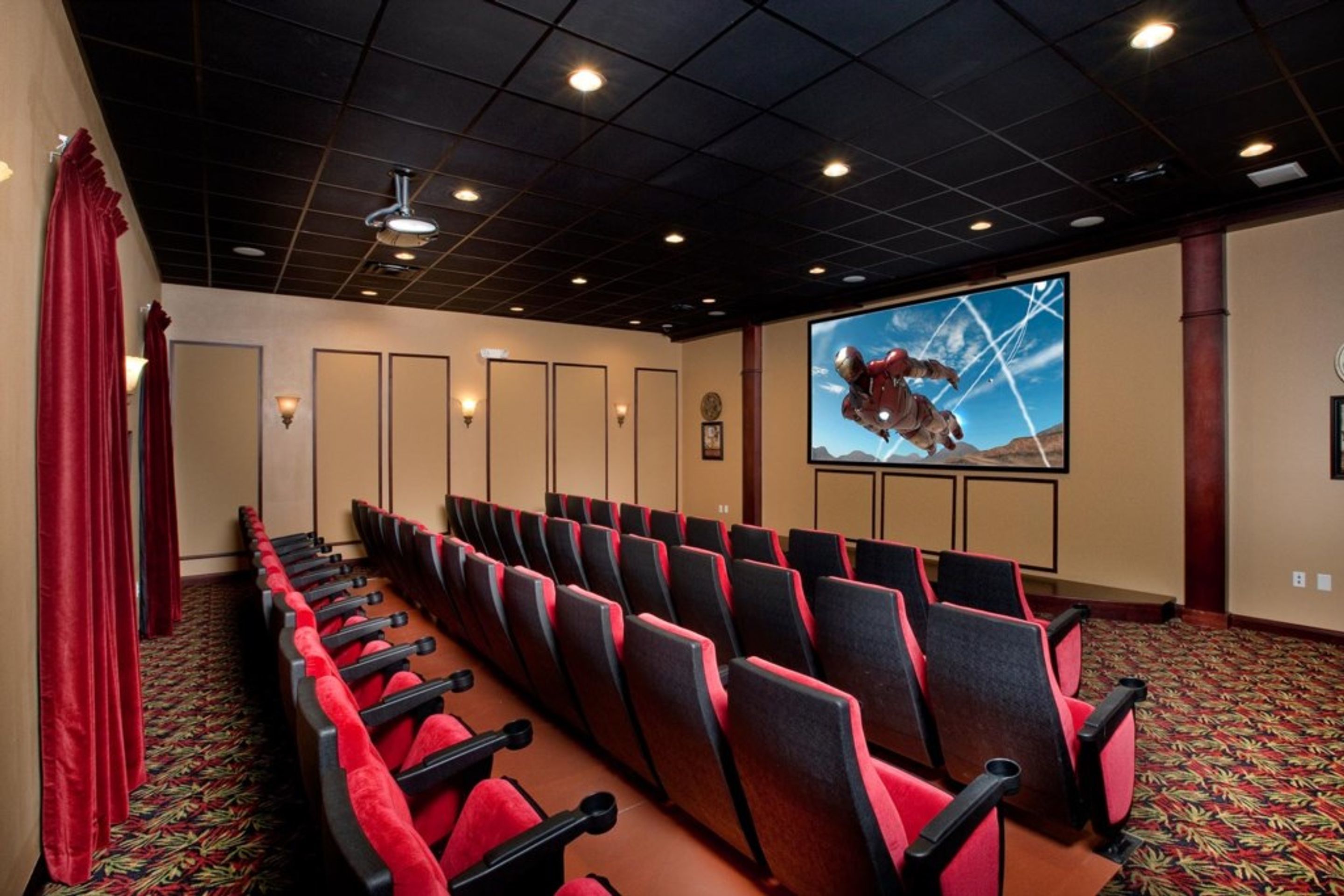 A conference room with rows of red and black chairs, a large screen displaying a person in a spacesuit, and a patterned carpet.