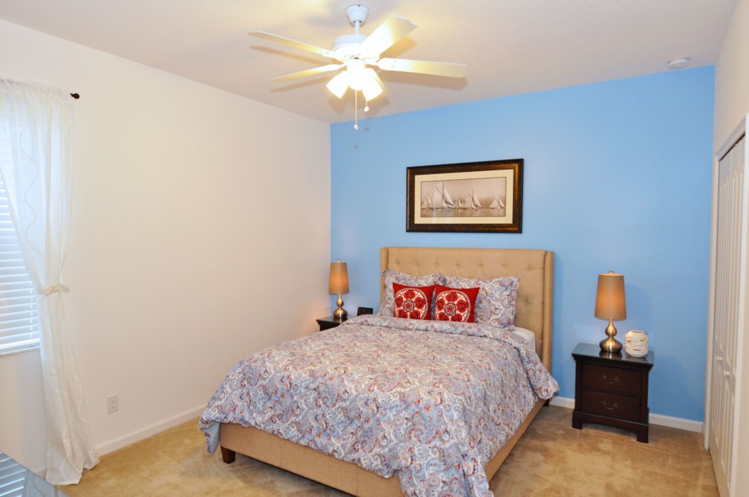 A bedroom with a bed, two bedside tables, a ceiling fan, and a framed picture on the wall.