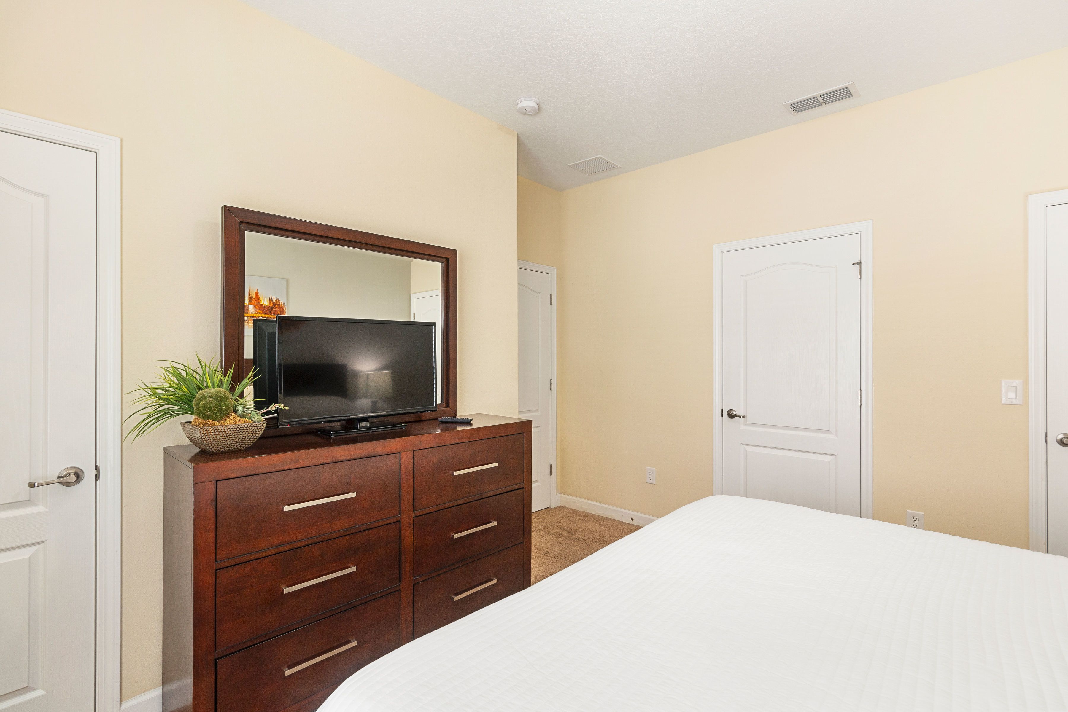 A bedroom with a bed, a dresser, a television, and a door.