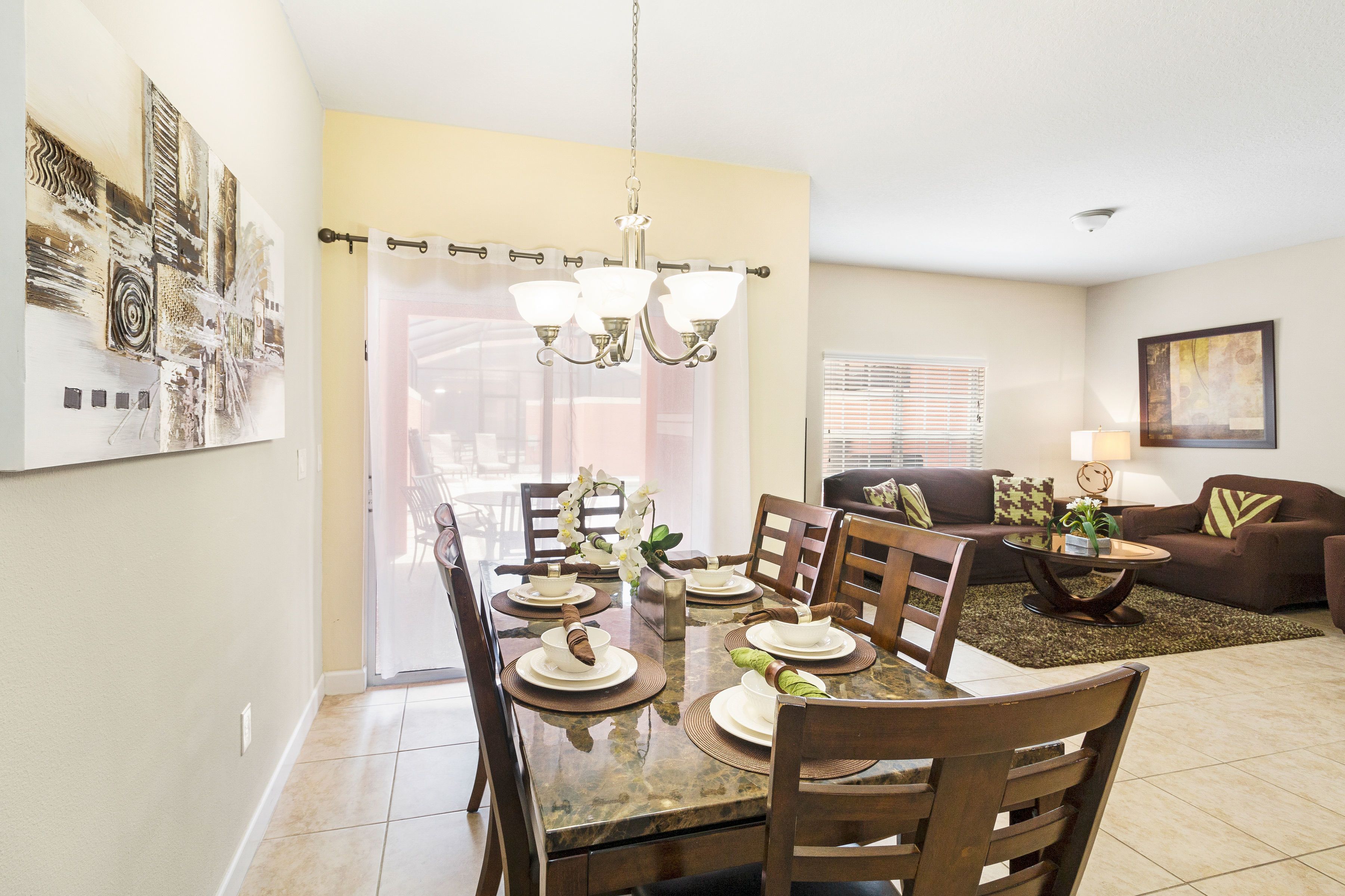 A dining area with a table set for four, chairs, a chandelier, and a sofa in the background.