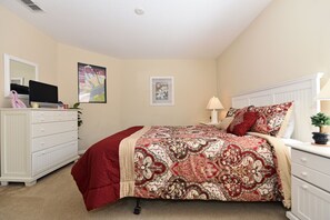 A bedroom with a bed, dresser, nightstand, lamp, and a poster on the wall.