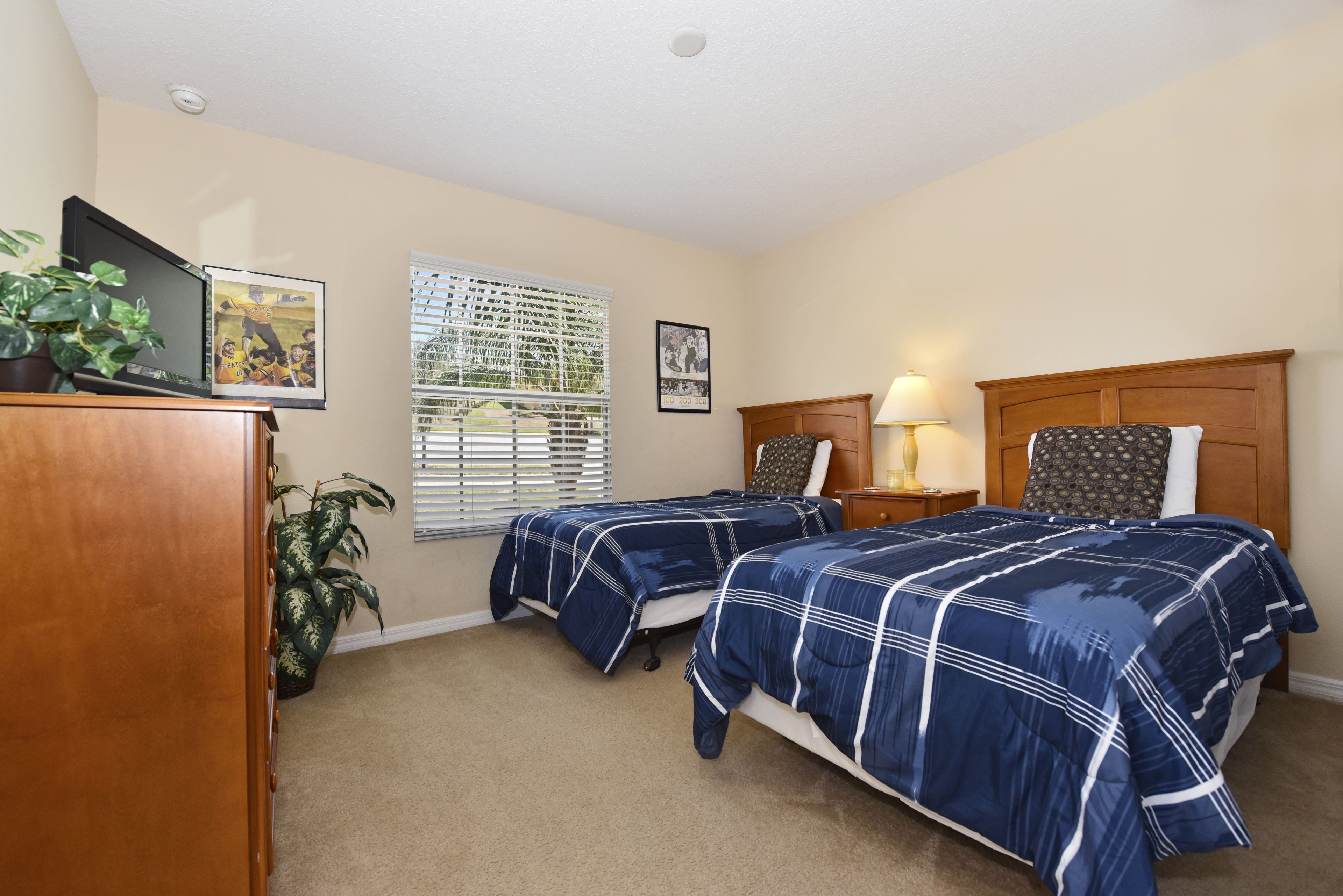 A bedroom with two beds, a desk, a lamp, and a plant.