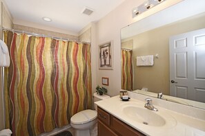 A bathroom with a striped shower curtain, a toilet, a sink with a mirror, and a door.
