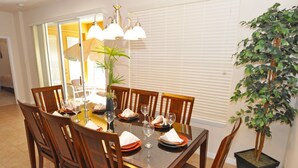 A dining area with a rectangular table set for six, surrounded by wooden chairs. There is a potted plant to the right of the table. - Watersong Resort 122 (Davenport)