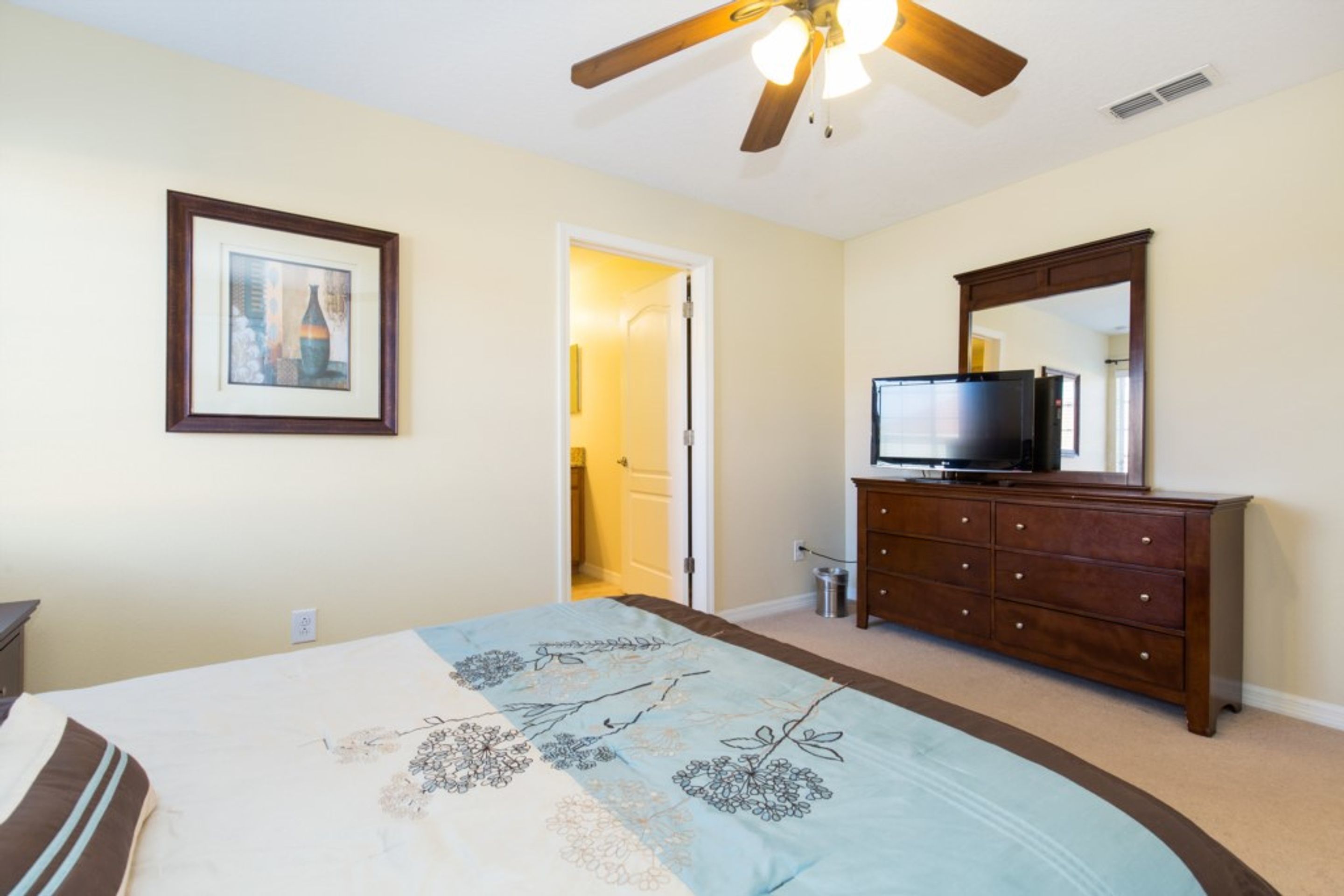 A bedroom with a bed, a dresser, a television, a ceiling fan, and a framed picture on the wall.