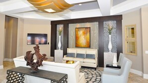 A modern living room with a white sofa, a coffee table, and a TV mounted on the wall. There are decorative vases and a large abstract painting on the wall. - Solterra 4380 (Davenport)