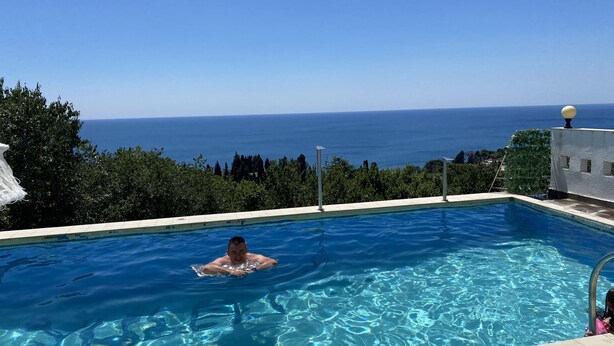 A swimming pool with clear blue water, surrounded by greenery and overlooking a scenic view of the sea. - Apartments & Rooms Rozana (Ulcinj)
