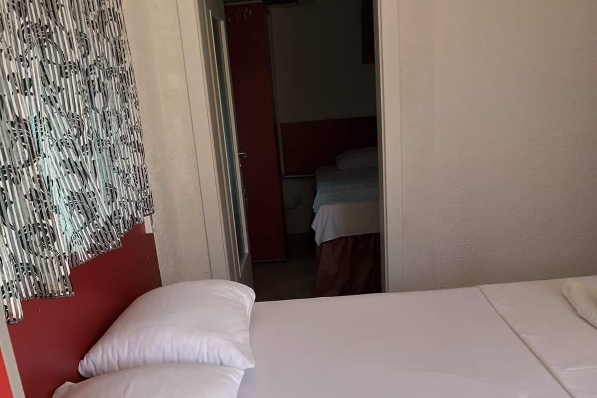 A single bed with white bedding in a room with a red accent wall and a patterned curtain.