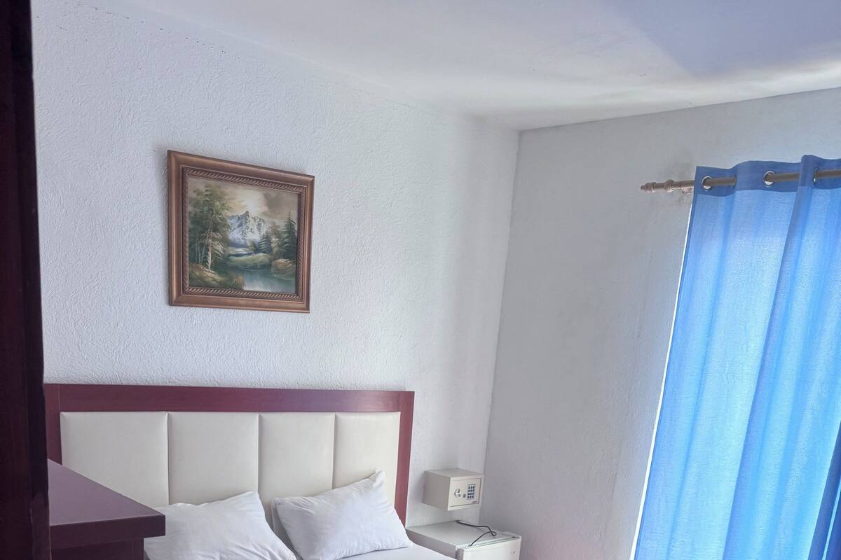 A hotel room with a large bed, a nightstand, a painting on the wall, and a window with curtains.