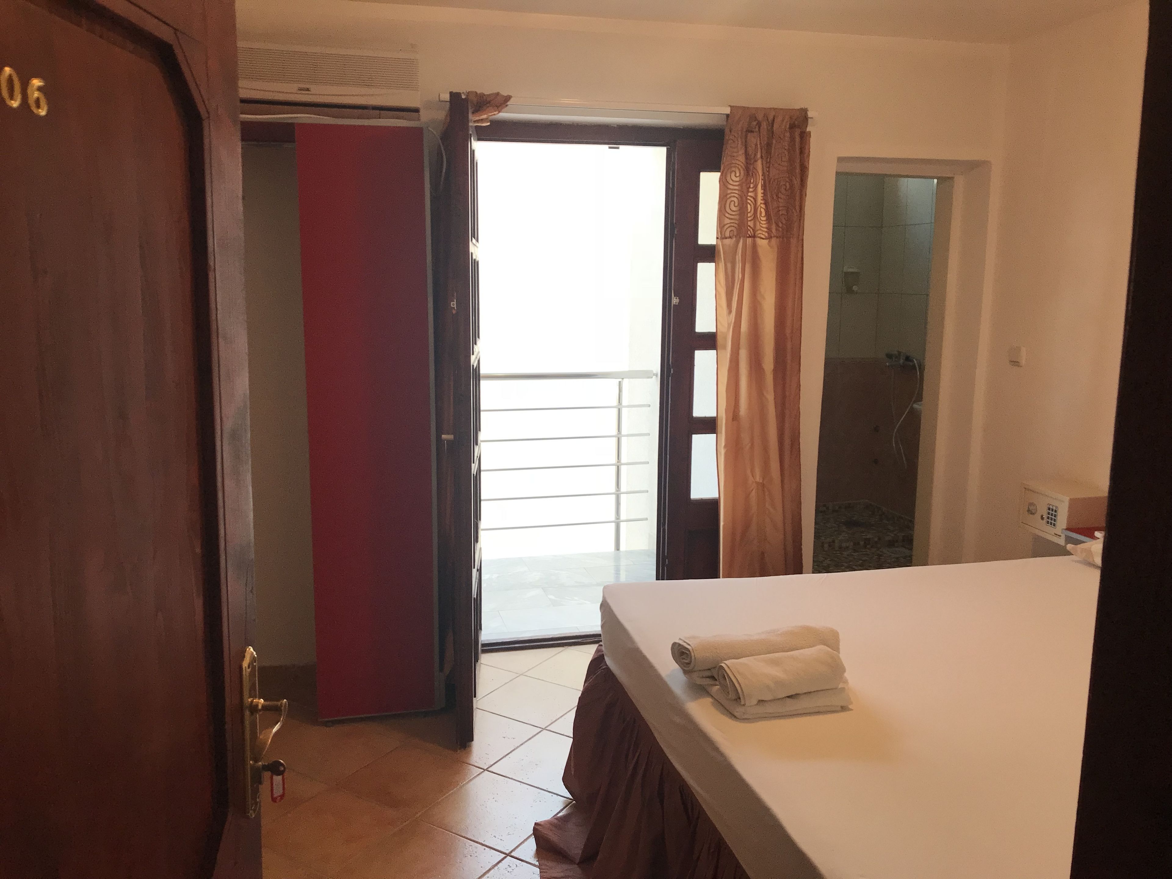 Ein Hotelzimmer mit Bett, einer Tür, einer roten Trennwand und Blick durch eine offene Tür.