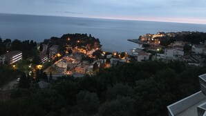 A coastal town at dusk with buildings, a prominent hilltop structure, and a view of the sea. - Apartments & Rooms Rozana (Ulcinj)