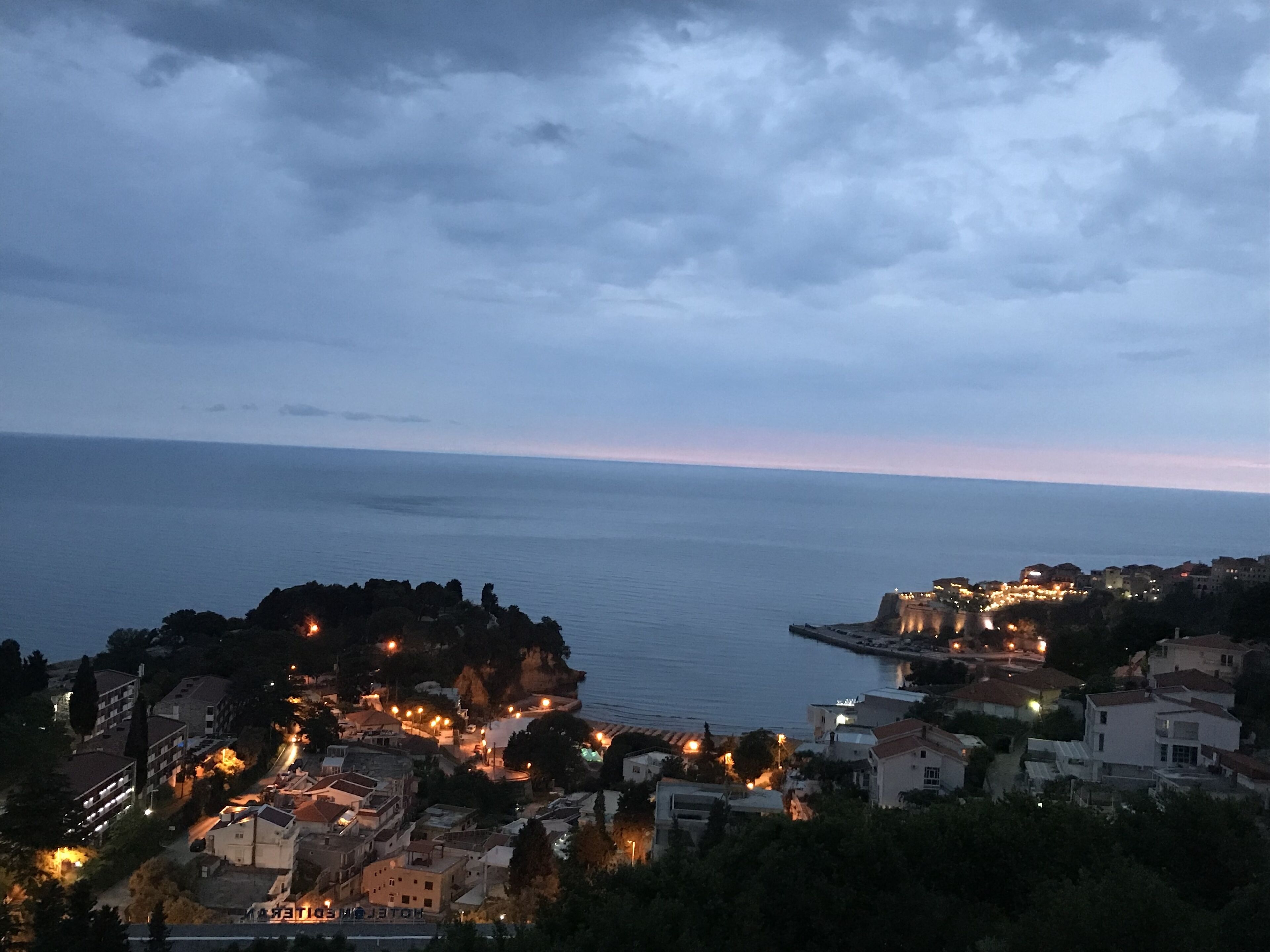 A coastal town at dusk with buildings and a rocky outcrop.