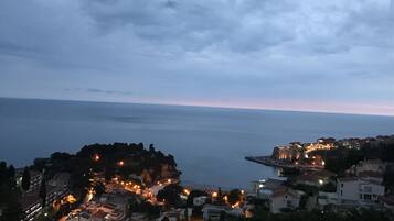 A coastal town at dusk with buildings and a rocky outcrop.
