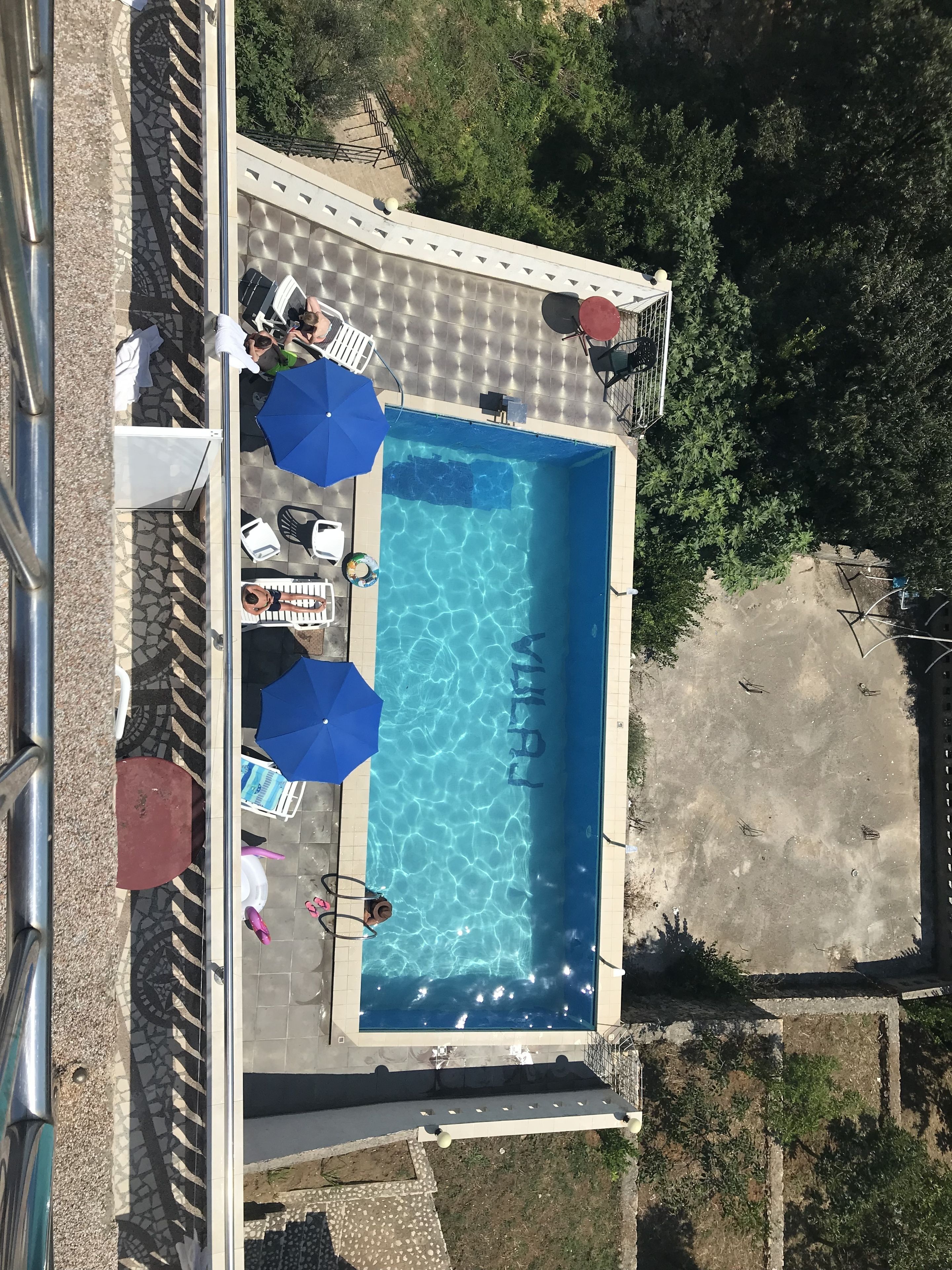An aerial view of a swimming pool with lounge chairs and umbrellas, surrounded by trees.