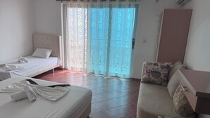 A hotel room with two beds, a sofa, a wardrobe, and a large window with curtains. - Apartments & Rooms Rozana (Ulcinj)