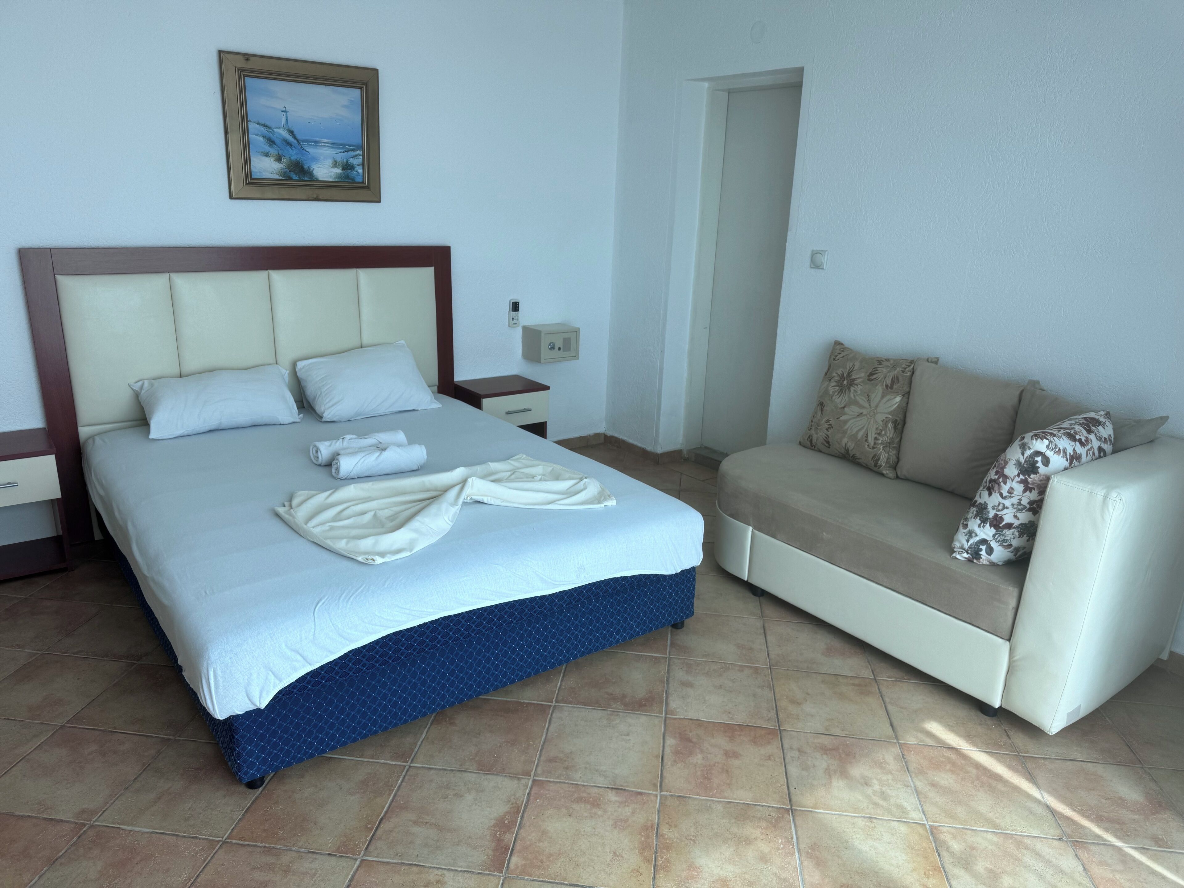 A hotel room with a bed, a nightstand, a sofa, and a painting on the wall.