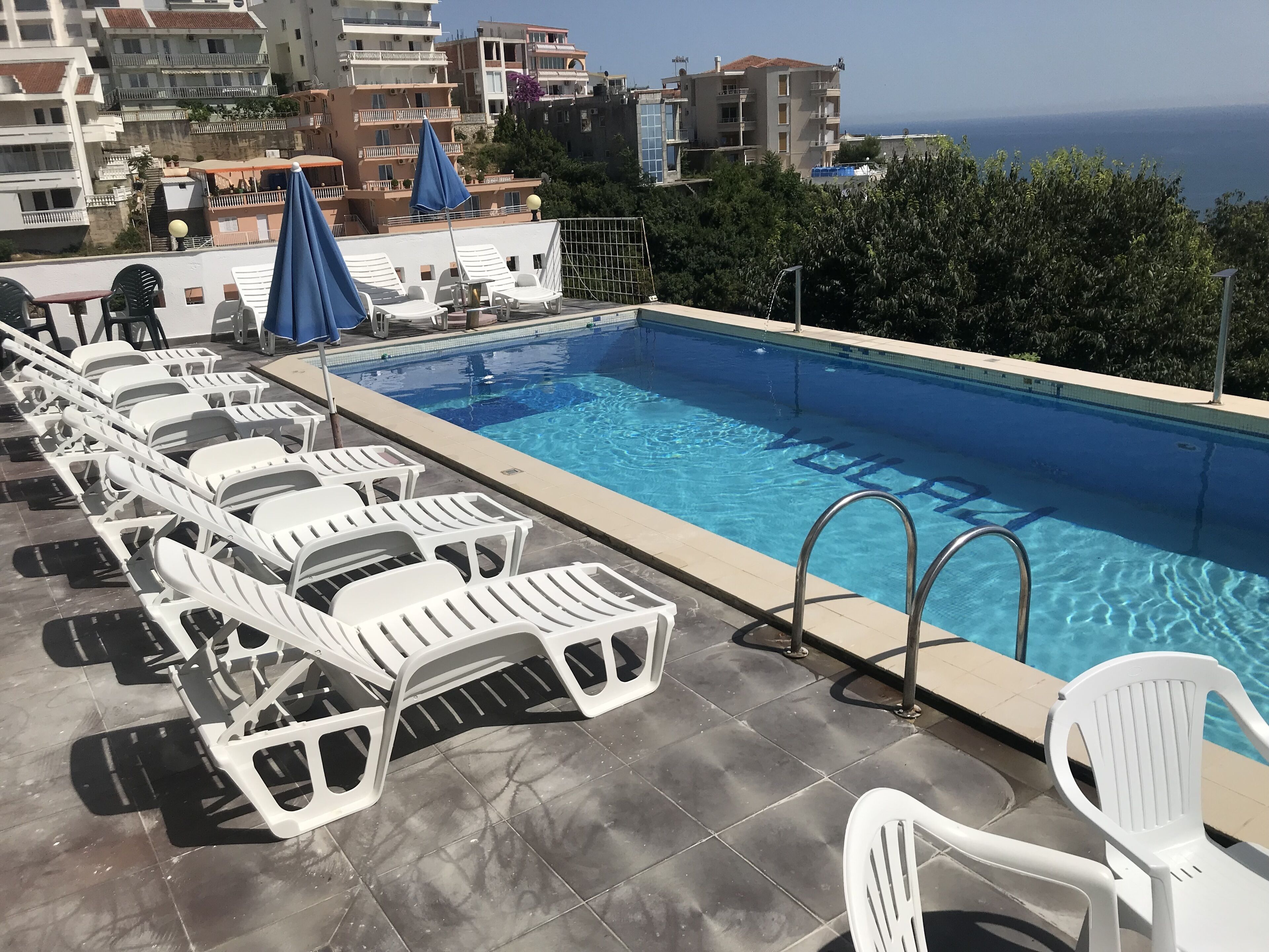 Une piscine bordée de chaises longues blanches, avec vue sur la mer.
