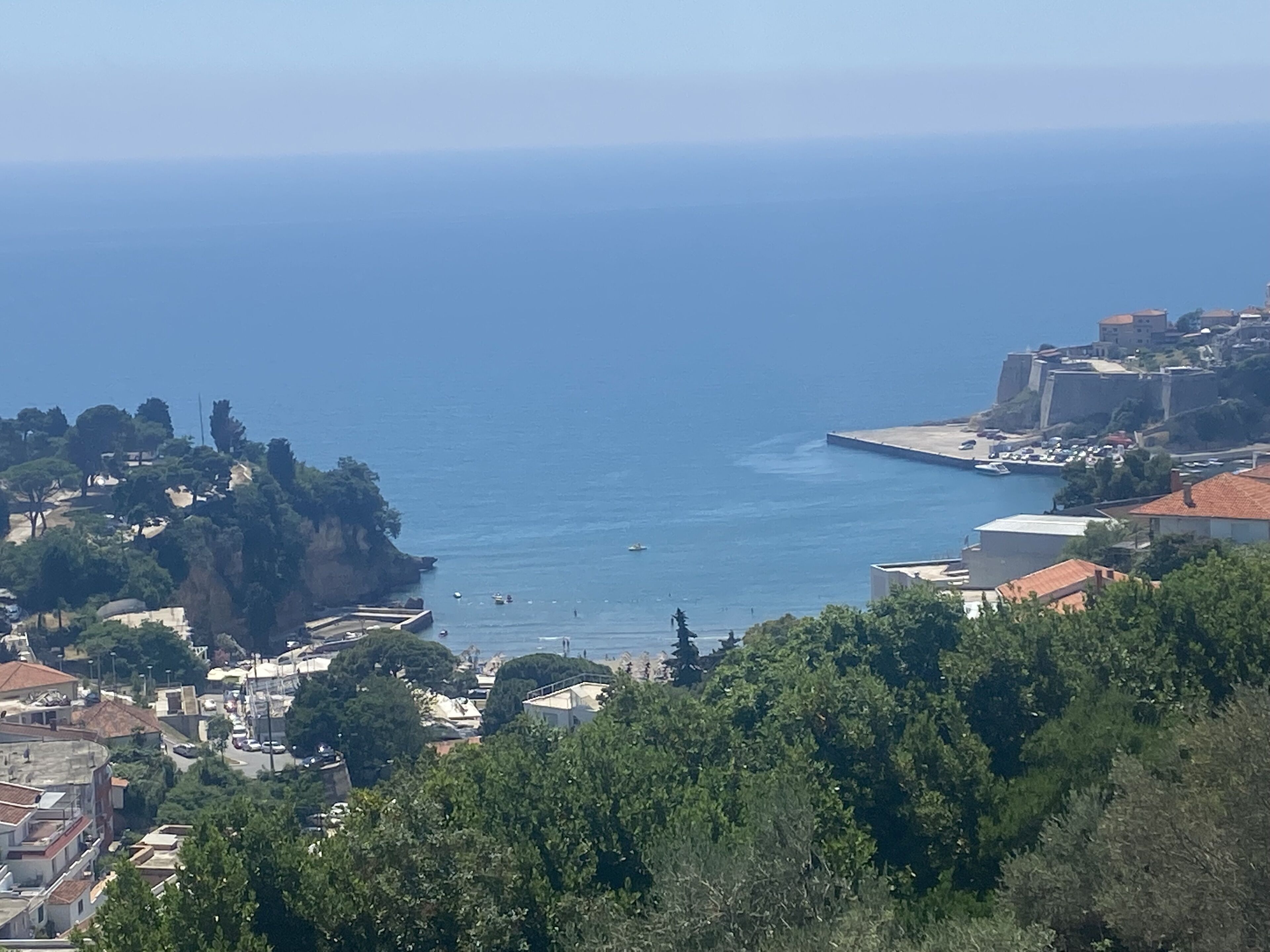 Une ville côtière avec des bâtiments, une mer bleue et limpide, et une falaise rocheuse.