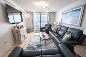 Relax in this stylish living room with a large sofa, armchair, and flat-screen TV, offering a serene ocean view.