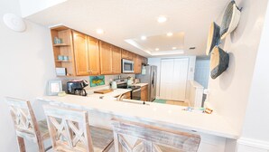 Cocina con armarios de madera, microondas, refrigerador y barra con taburetes.