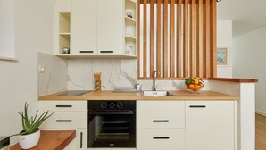 A compact kitchen with white cabinetry, a wooden countertop, a built-in oven, and a fruit bowl.