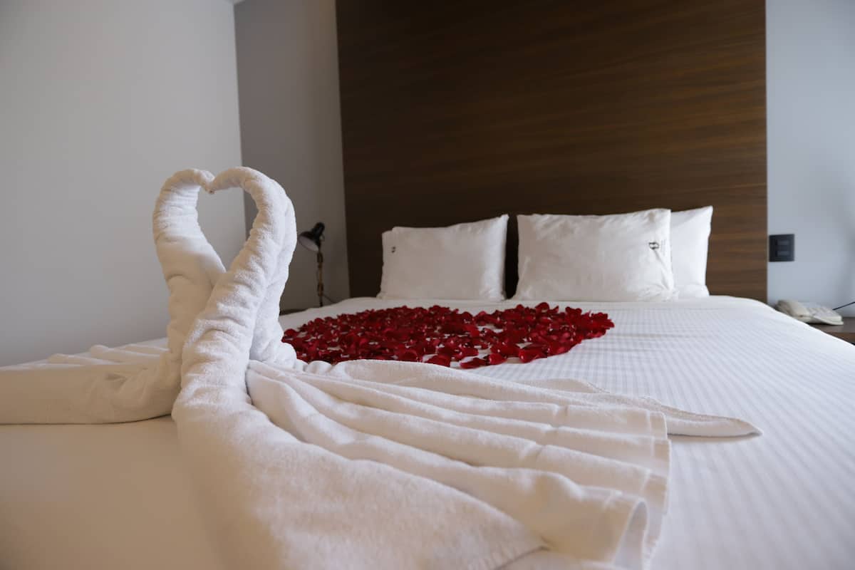 A neatly made bed with a heart-shaped arrangement of rose petals and a towel sculpture.